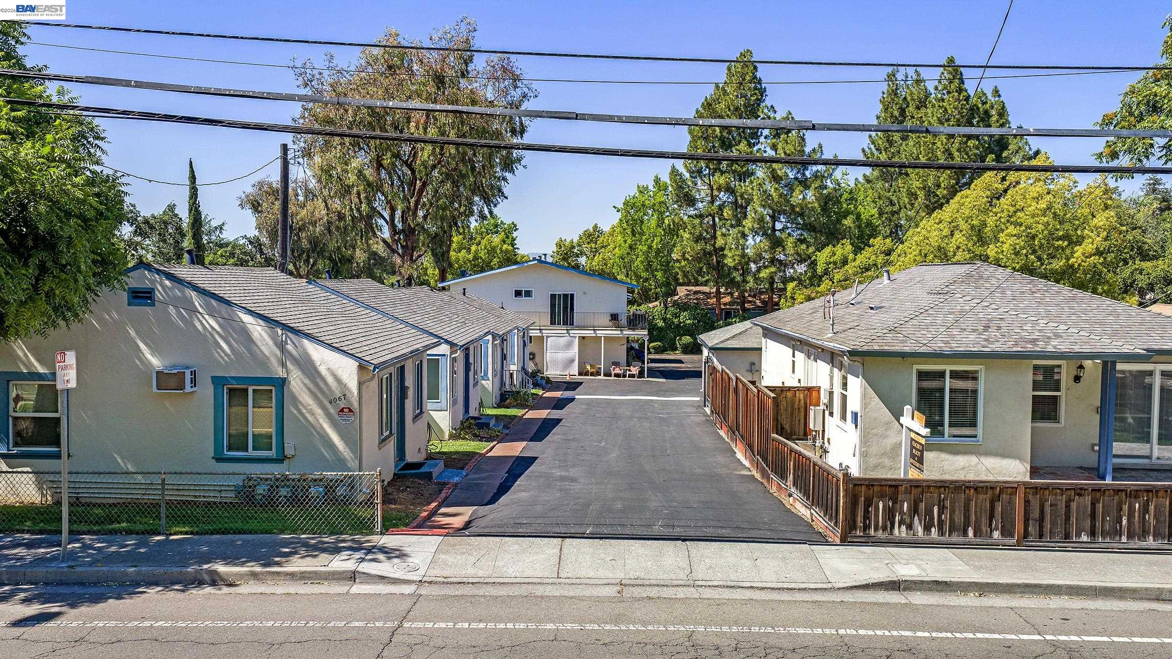 Multi-unit property with homes lining a central driveway, mature trees, and fenced front areas.