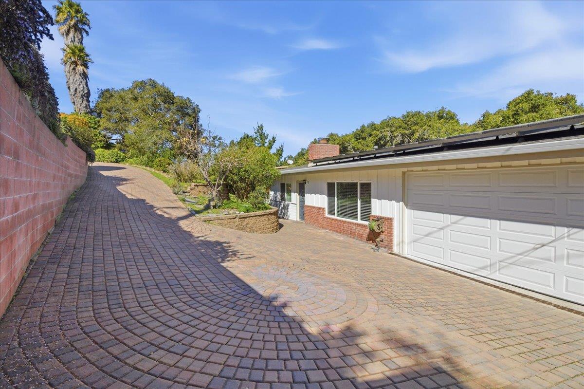 House with a white garage and curved brick-paver driveway beside a red retaining wall.