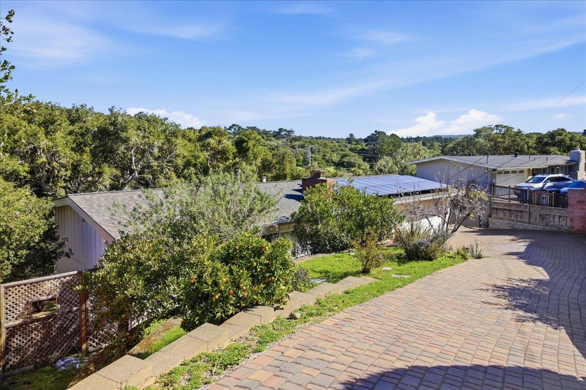 Home with a broad brick-paved driveway, rooftop solar panels, and wooded hills beyond.