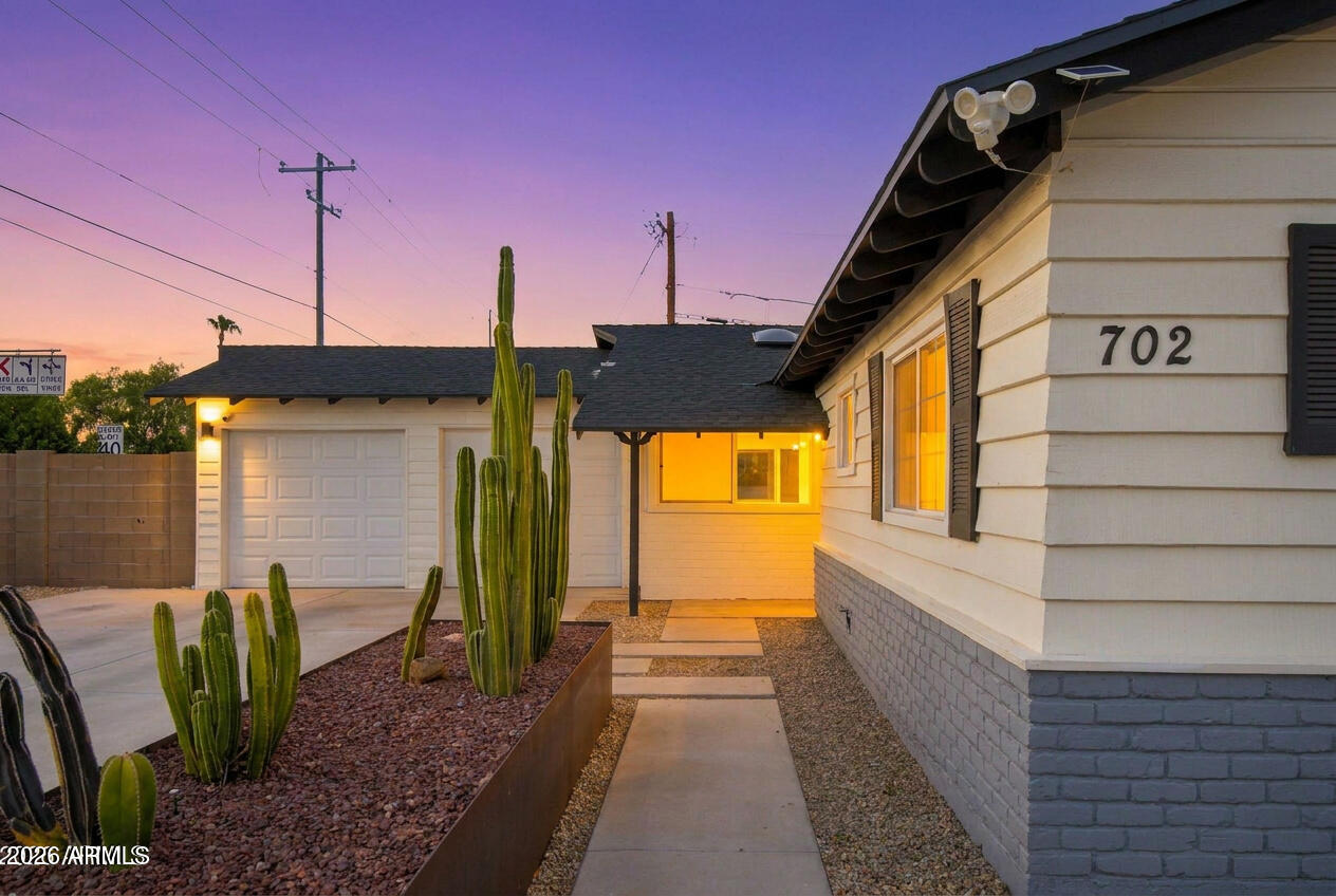 Home exterior at dusk with tall cacti, a paved walkway, and address number 702.