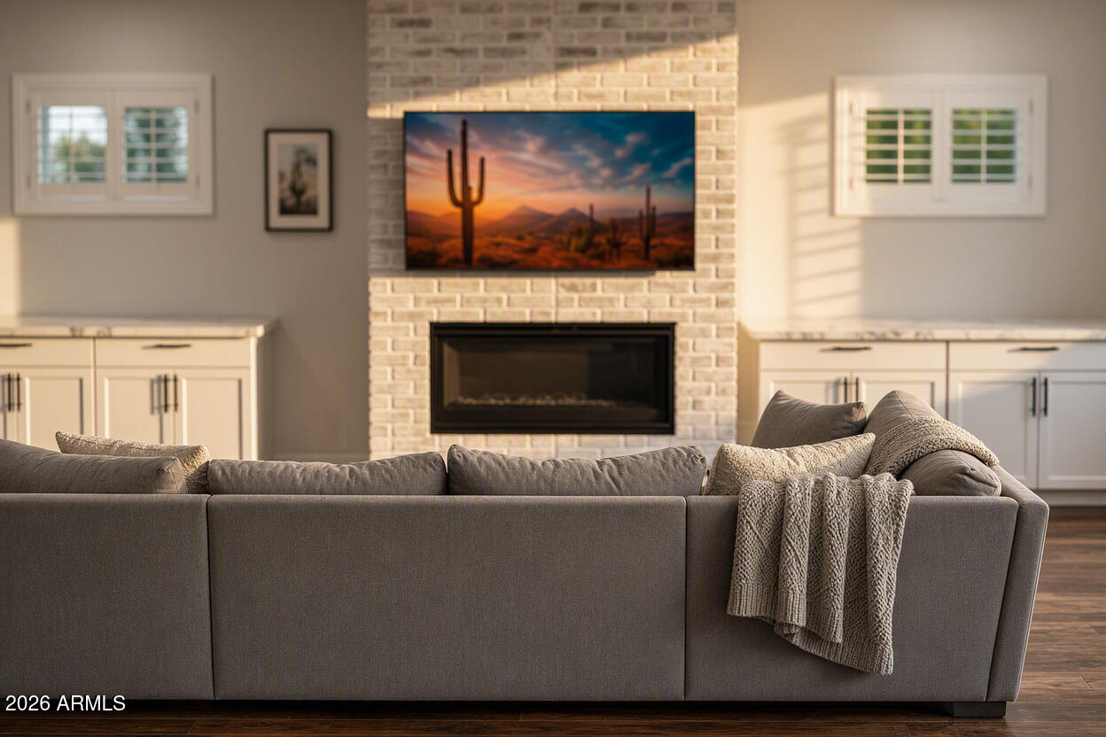 Living room with a gray sofa, white brick fireplace, and television showing a desert sunset.