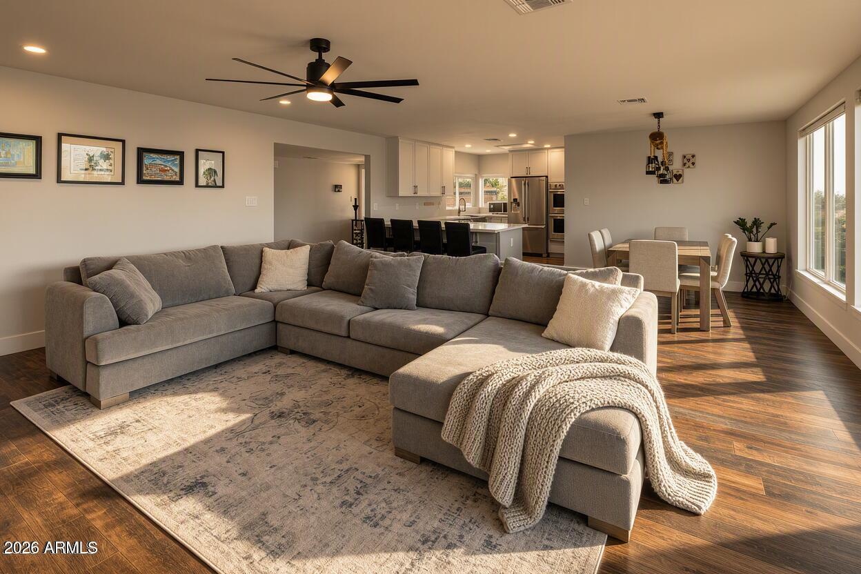 Open-plan living room with gray sectional, wood floors, and kitchen and dining area beyond.