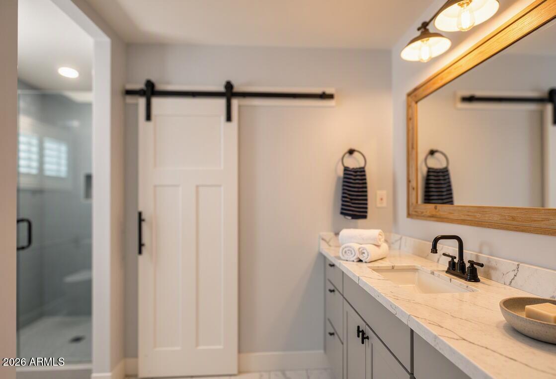 Bathroom vanity with a marble-look counter, wood-framed mirror, barn door, and glass shower.