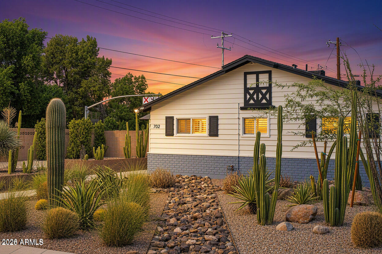 Single-story home with desert landscaping and tall cacti at dusk.