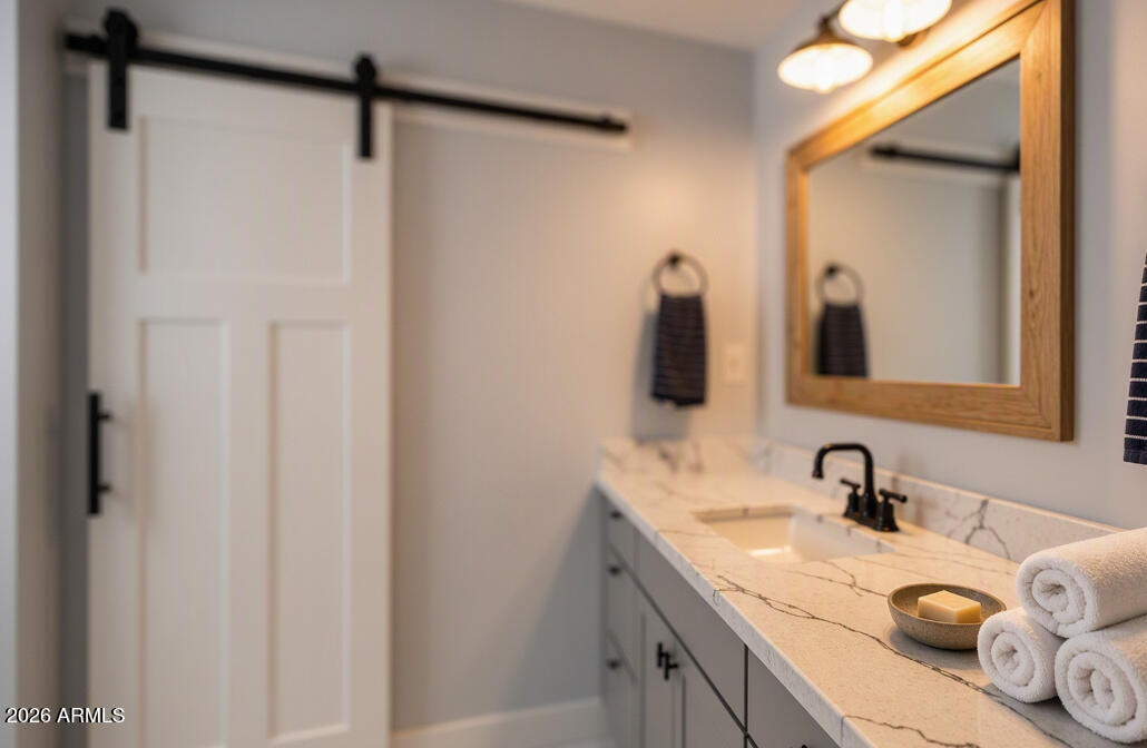 Bathroom vanity with marble-look counter, black faucet, wood-framed mirror, and rolled towels.