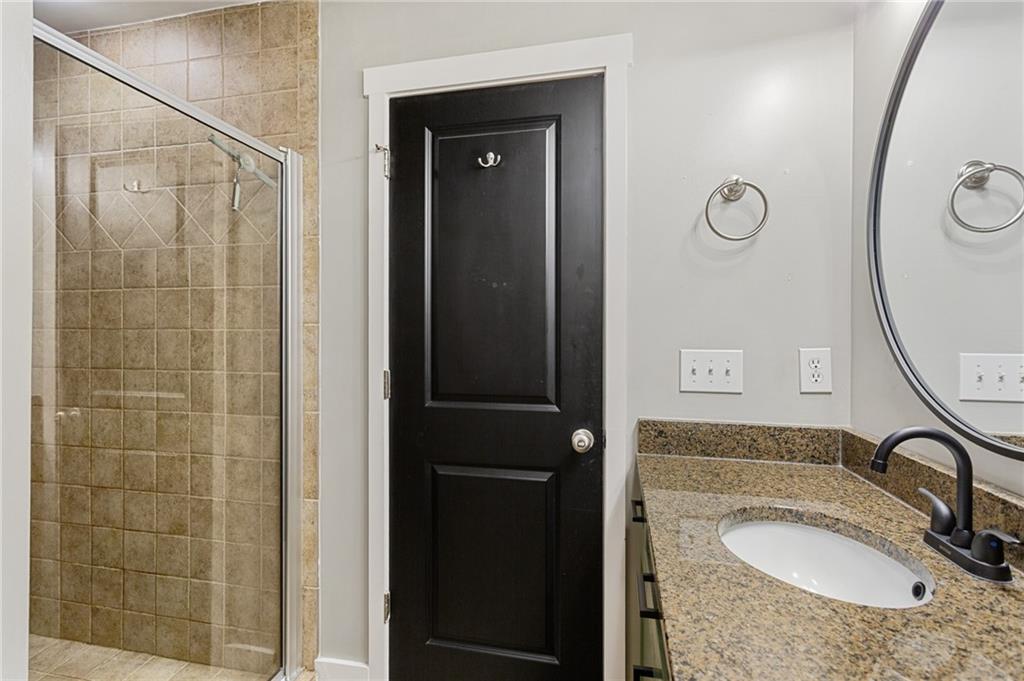 Bathroom with a beige-tiled glass shower, granite vanity, oval sink, and black paneled door.