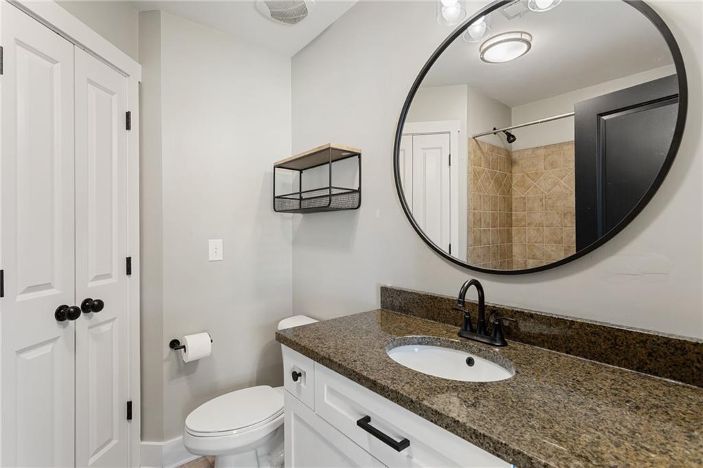 Bathroom with granite vanity, oval mirror, white cabinetry, and tan tiled shower.