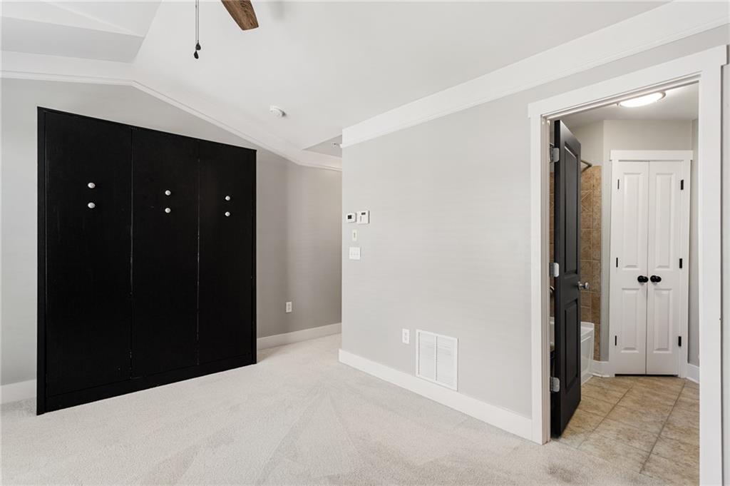 Empty carpeted bedroom with a large black built-in wardrobe and an open bathroom doorway.