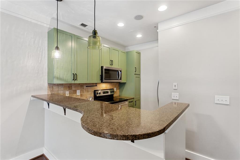 Kitchen with sage-green cabinets and a curved granite peninsula counter.