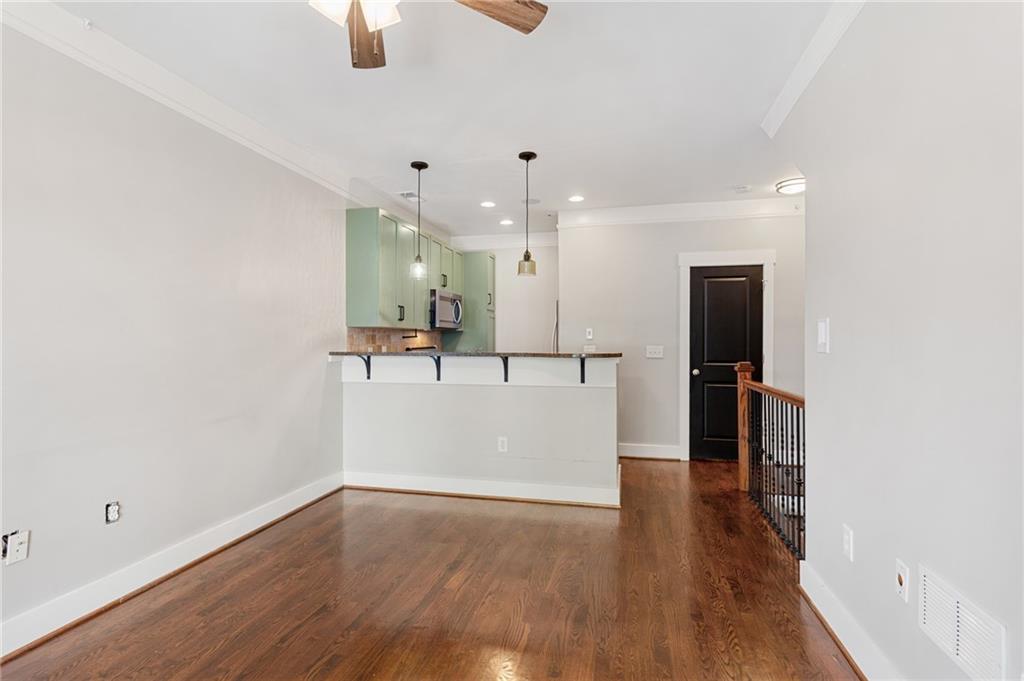 Empty living area with hardwood floors and an open kitchen with pale green cabinets.
