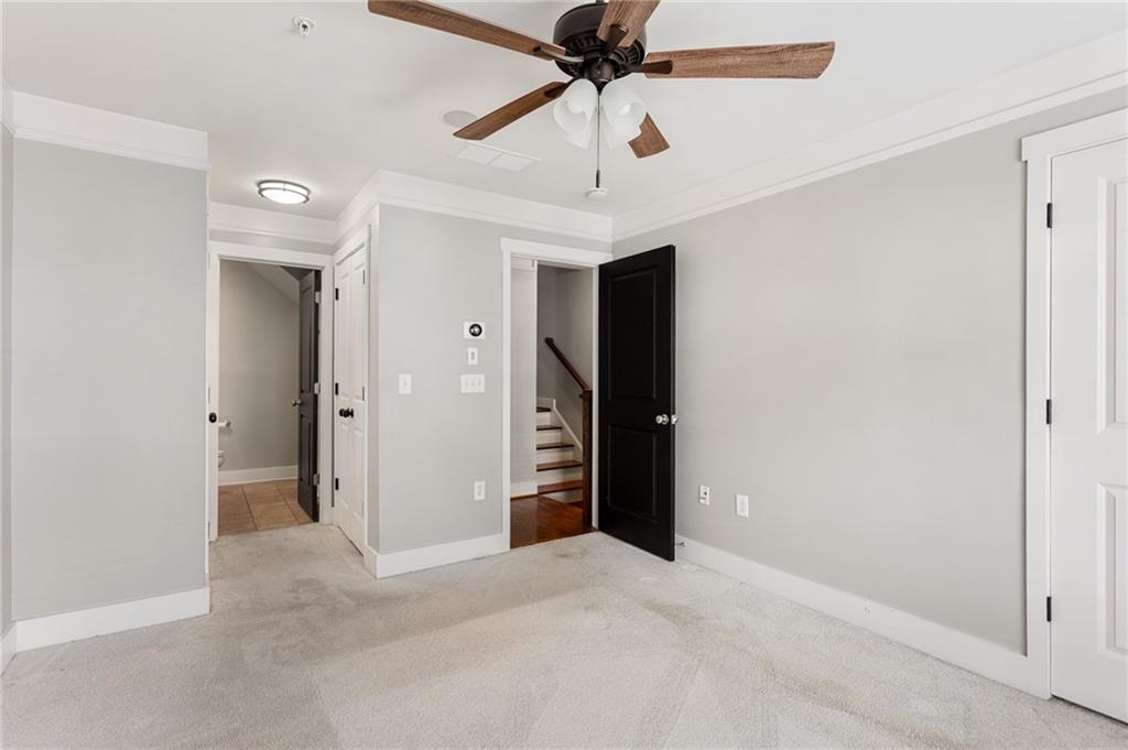 Empty carpeted room with a wood-blade ceiling fan and an open doorway to stairs.
