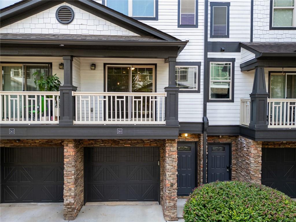 Townhome exterior with a covered balcony, stone columns, dark garage doors, and unit number 260.