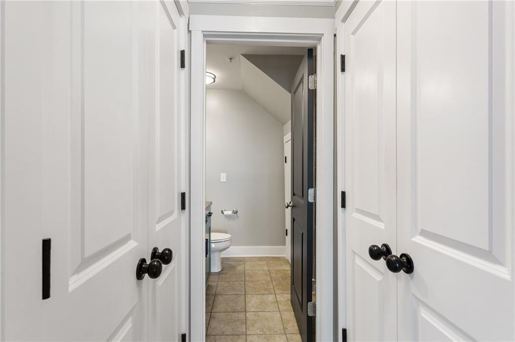 Bathroom with a tiled floor and sloped ceiling, viewed through open doors.