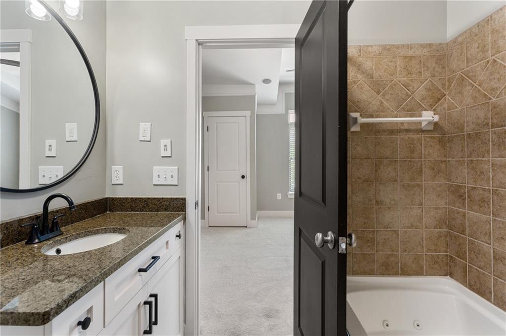 Bathroom with a granite-topped vanity and tan tiled bathtub surround.