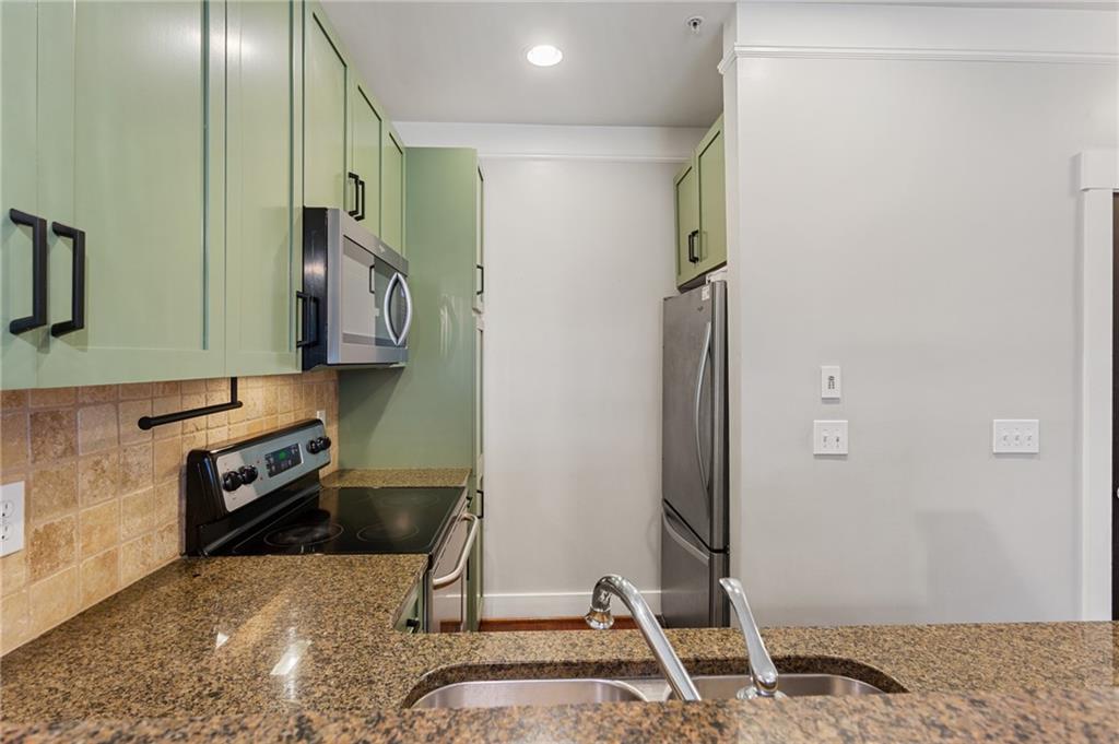 Compact kitchen with pale green cabinets, granite counters, stainless steel appliances, and a double sink.