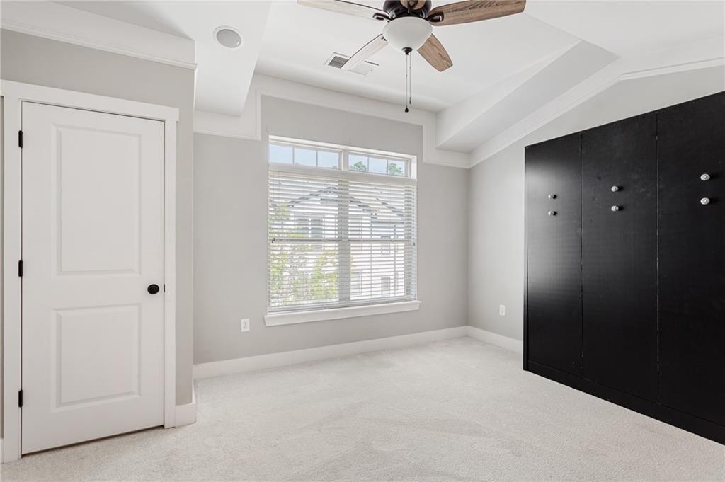 Empty bedroom with a large blinded window, ceiling fan, and black built-in wardrobe.