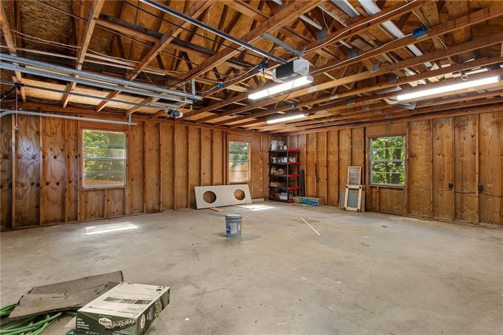 Unfinished garage with exposed wood framing, ceiling rafters, windows, and a concrete floor.