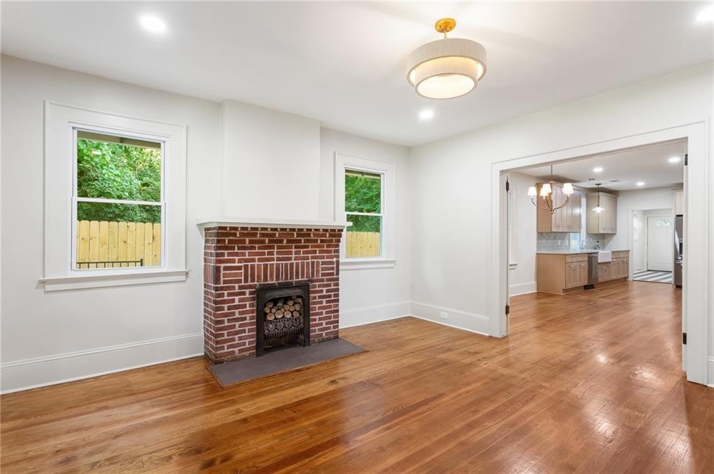 Unfurnished living room with a brick fireplace, hardwood floors, and a wide opening to the kitchen.
