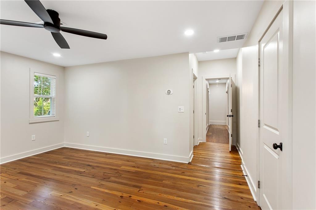 Empty bedroom with hardwood floors, a ceiling fan, and a hallway leading to other rooms.