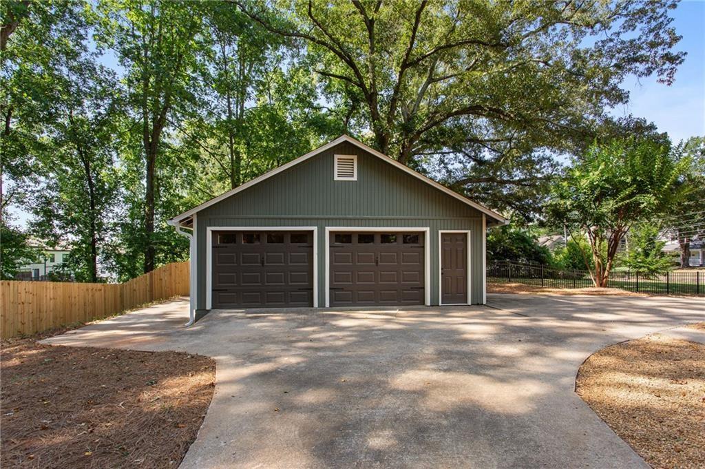 Detached gray garage with two doors and a wide concrete driveway beneath mature trees.