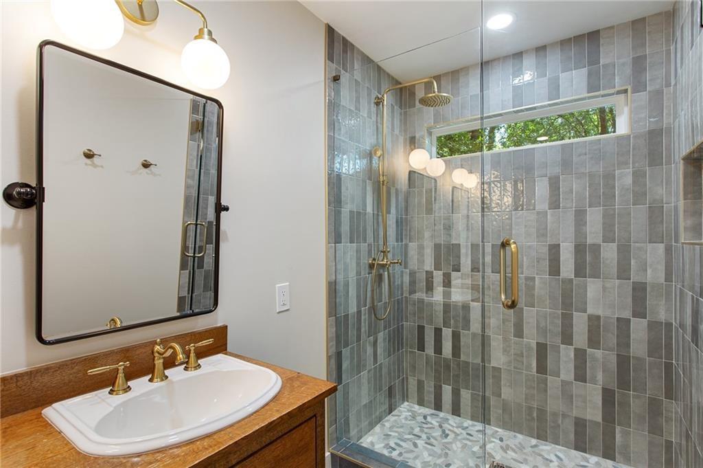 Bathroom with a wood vanity and a glass-enclosed gray-tiled shower with brass fixtures.