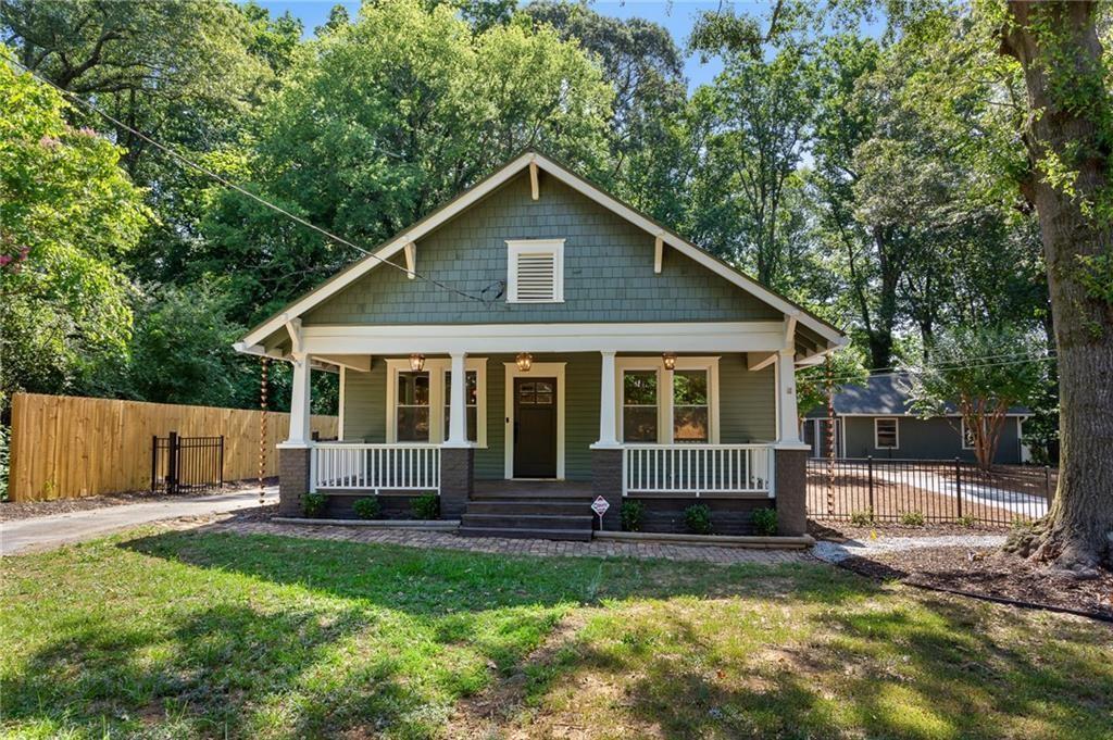 Sage-green bungalow with a white-railed front porch beneath mature trees.