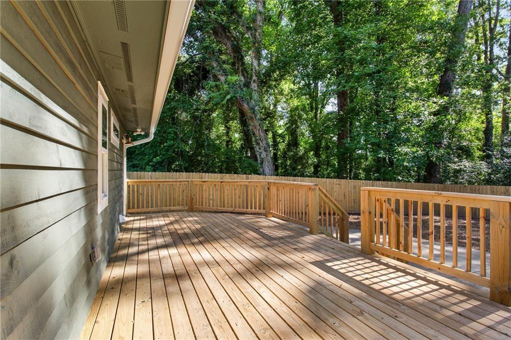 Raised wooden deck with railings beside the home, overlooking a leafy wooded backyard.