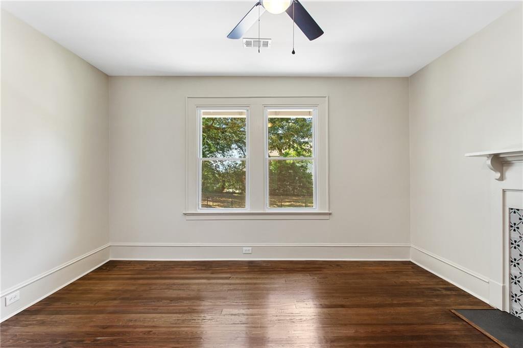 Empty room with dark hardwood floors, a ceiling fan, and two windows overlooking trees.