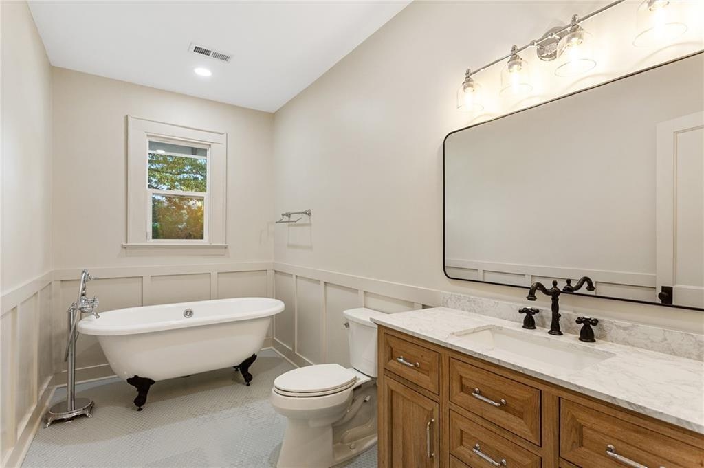 Bathroom with a clawfoot tub beneath a window and a wood vanity with a marble countertop.