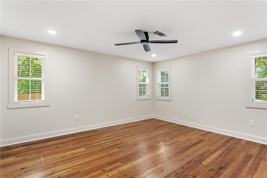 Empty room with hardwood floors, multiple windows, and a ceiling fan.
