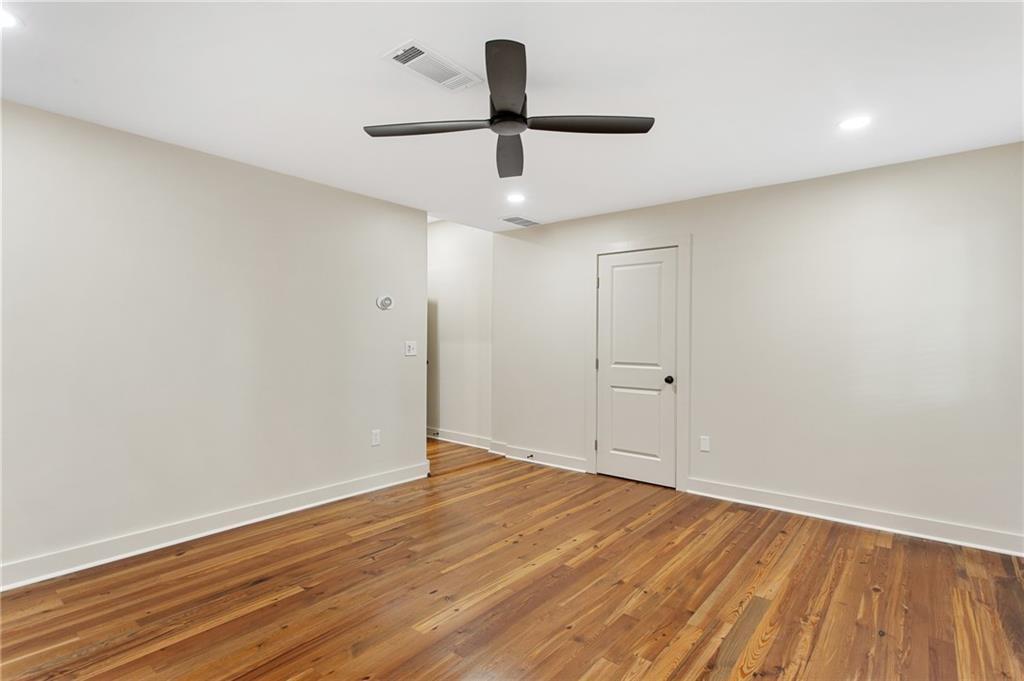 Empty room with hardwood floors, a dark ceiling fan, and a white door.