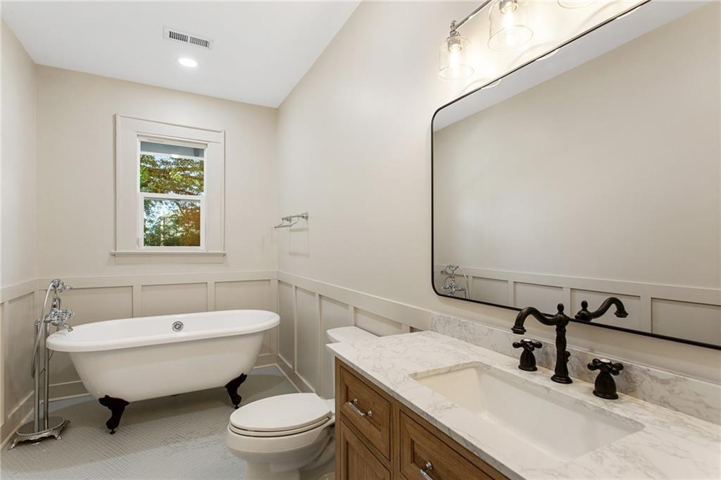 Bathroom with a clawfoot tub, marble-topped wood vanity, and paneled wainscoting