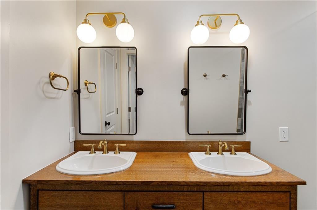 Bathroom double vanity with a warm wood countertop, black-framed mirrors, and brass fixtures.