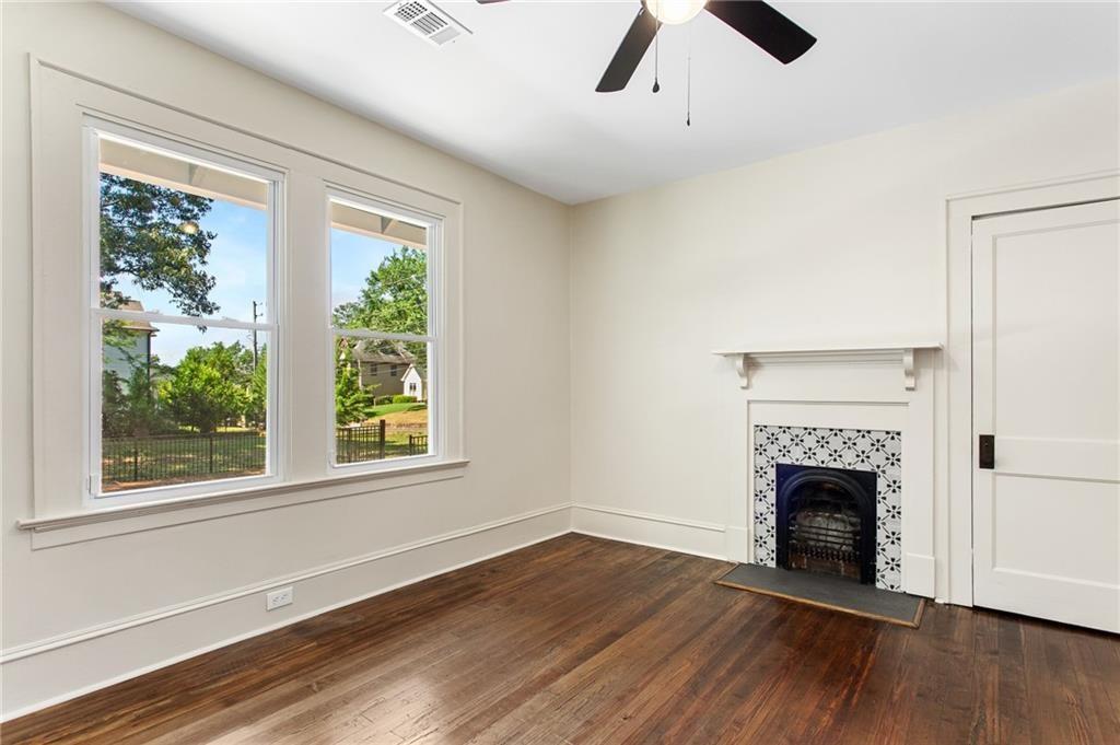 Vacant room with hardwood floors, two tall windows, and a decorative tiled fireplace.