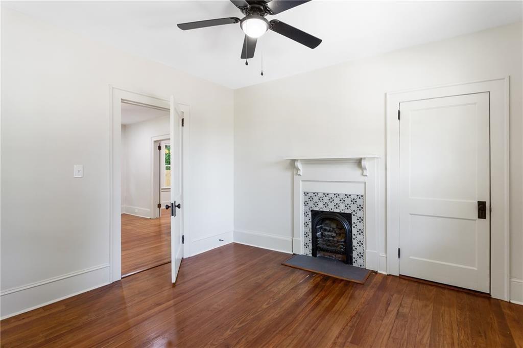 Vacant room with hardwood floors, a tiled fireplace, and a black ceiling fan.