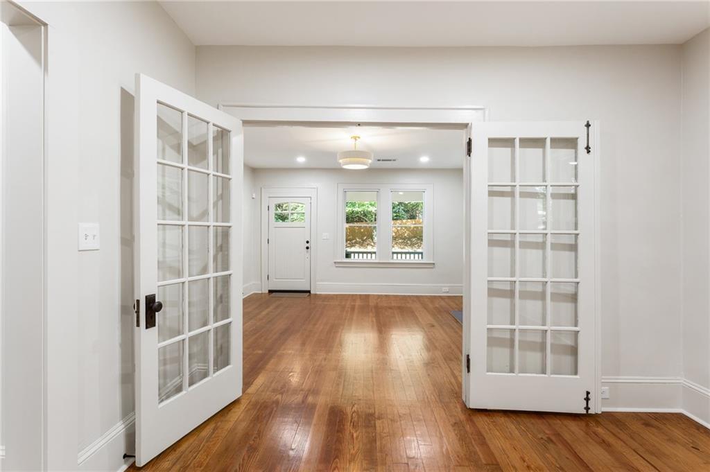 Open French doors lead into a bright, vacant room with hardwood floors and two windows.