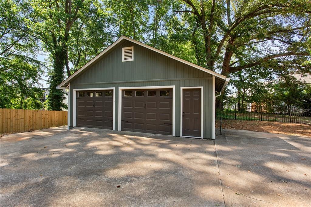 Detached two-car garage with gray-green siding, separate entry door, and a broad concrete driveway.