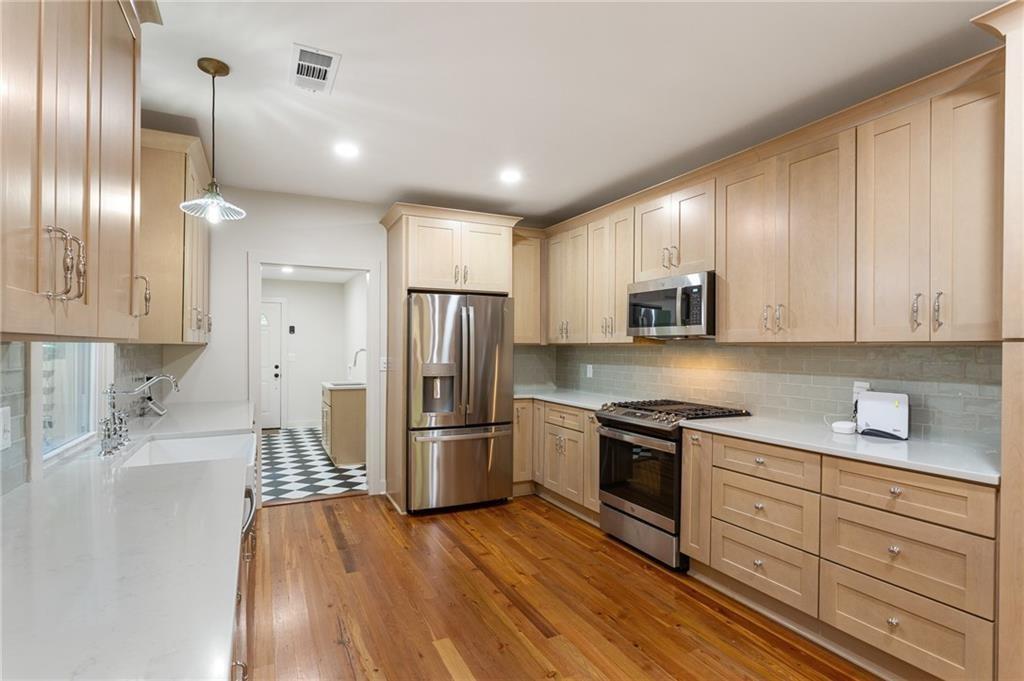 Kitchen with light wood cabinetry, stainless steel appliances, white counters, and hardwood floors.