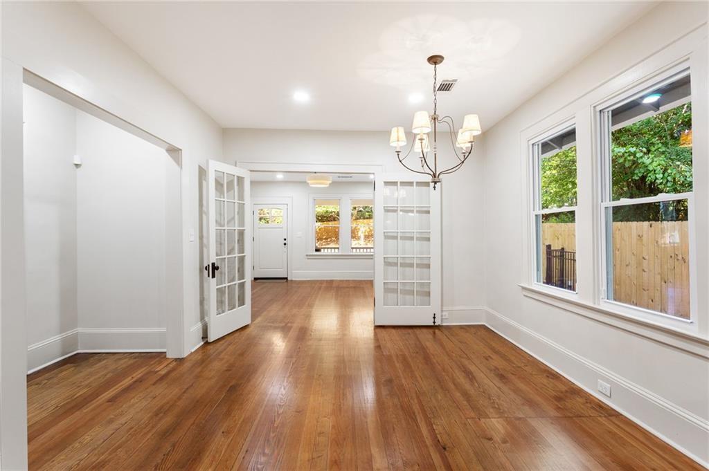 Empty dining room with hardwood floors, a chandelier, French doors, and large windows overlooking a fenced yard.