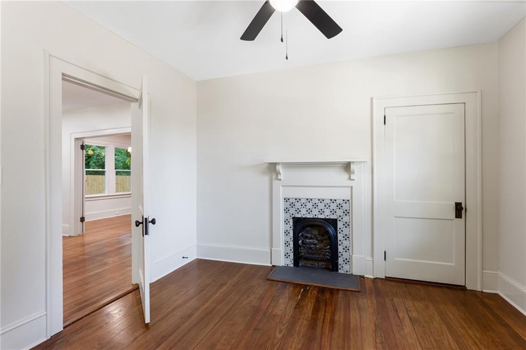 Empty room with hardwood floors, ceiling fan, and a fireplace framed by patterned tile.