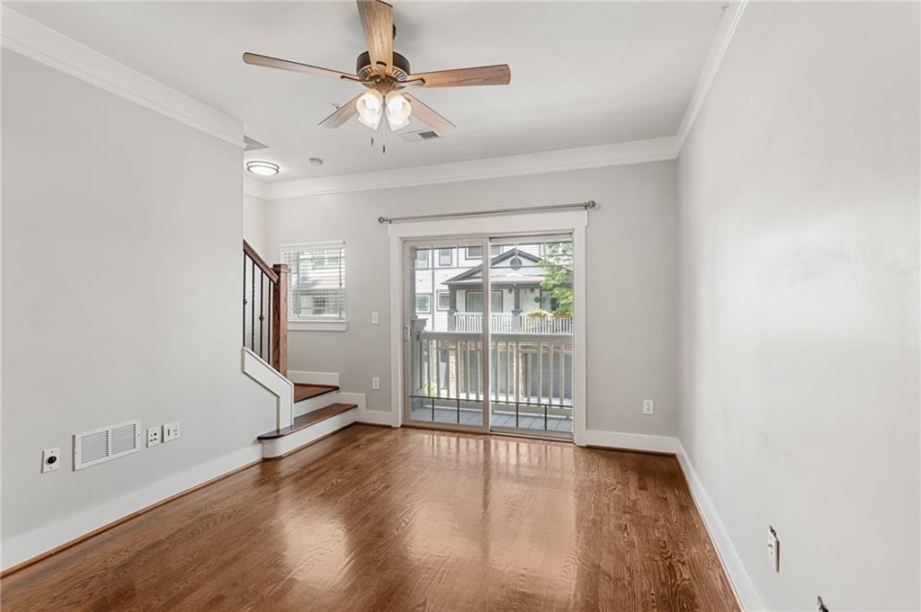 Empty living room with hardwood floors, a ceiling fan, and sliding doors to a balcony.