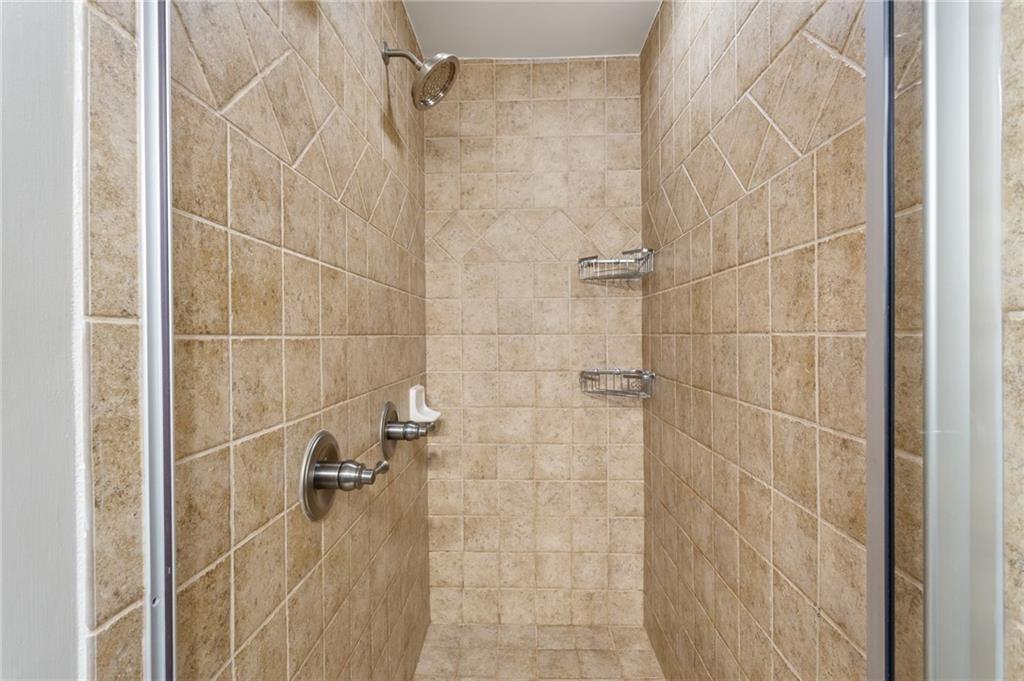 Walk-in shower with beige stone tile, chrome fixtures, and two wire storage racks.