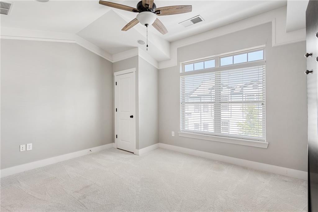 Empty bedroom with light carpet, a large window with blinds, and a ceiling fan.