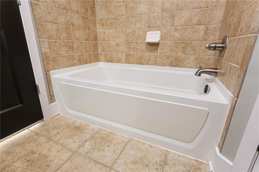 Bathroom with a white bathtub, tan tile walls and floor, and chrome fixtures.