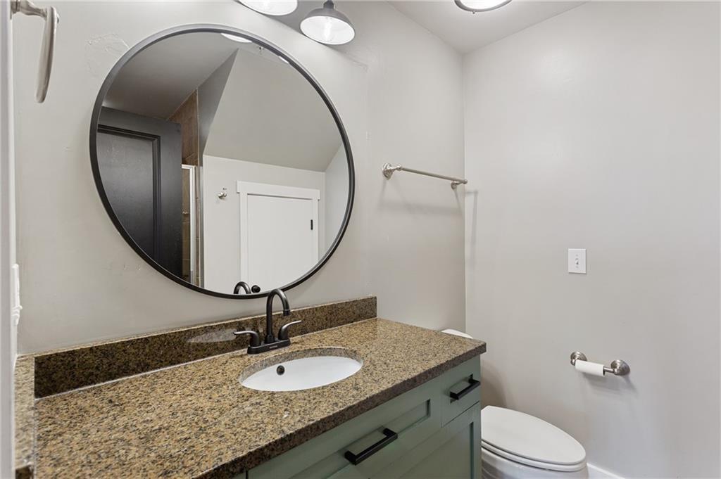 Bathroom vanity with speckled granite countertop, dark faucet, green-gray cabinets, and a large round mirror.