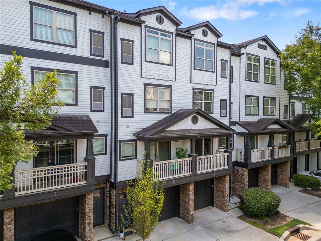 Attached white townhomes with dark trim, covered porches, stone supports, and ground-level garages.