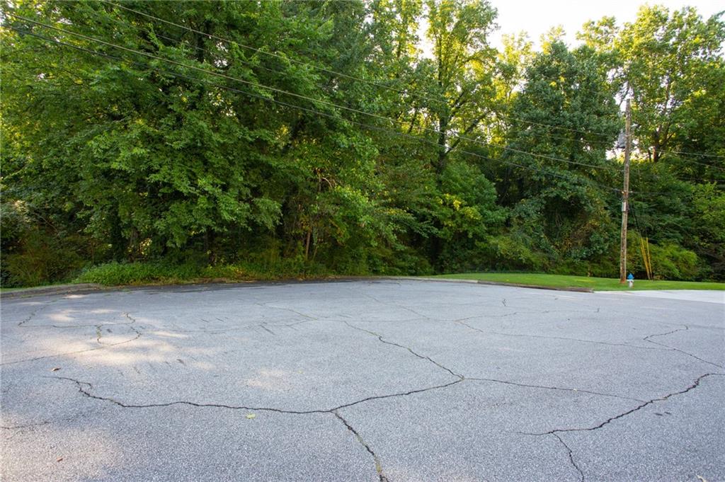 Cracked asphalt road bordered by dense trees and overhead utility lines.