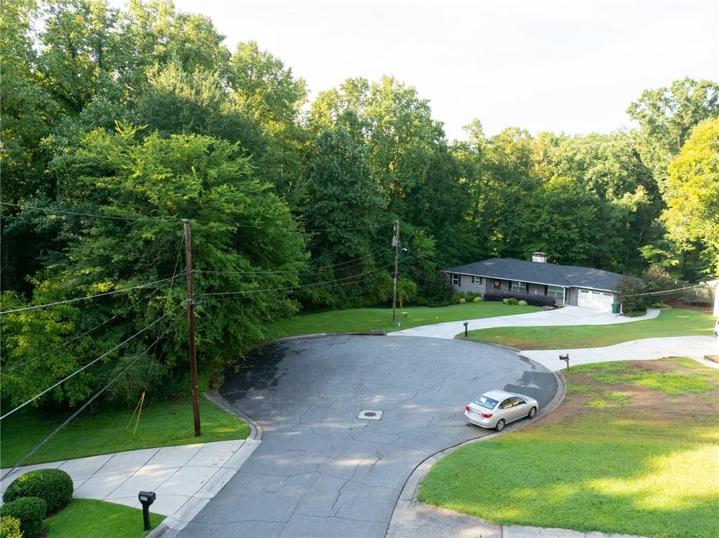 Elevated view of a ranch house on a wooded cul-de-sac with a broad driveway.