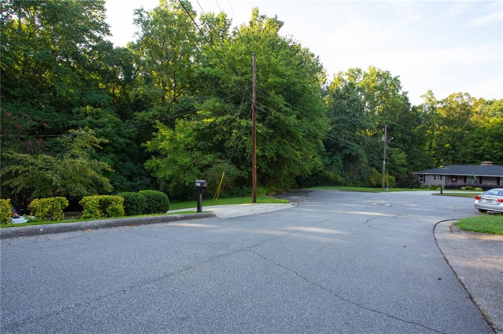 Residential street corner with dense trees, a mailbox, and a single-story house across the road.