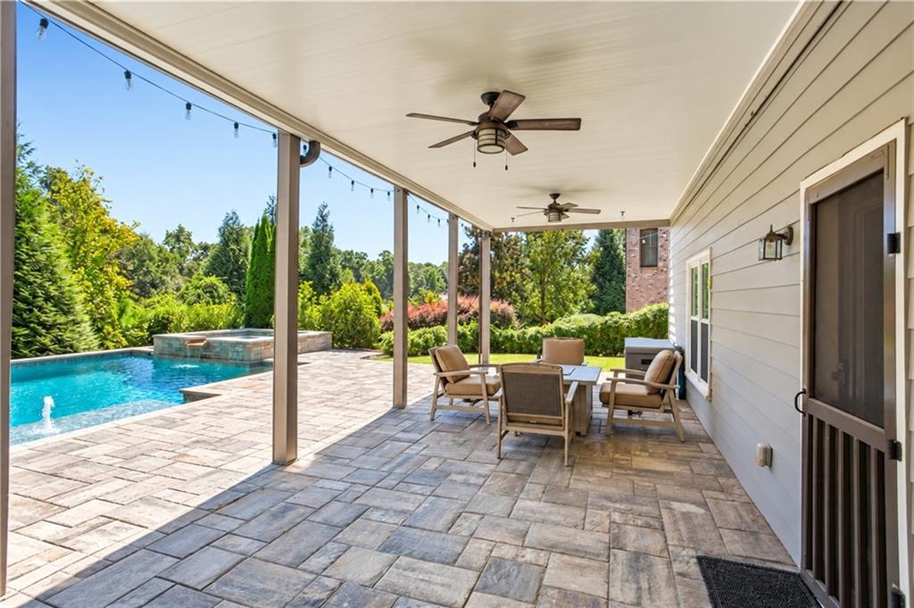 Covered stone-paver patio with ceiling fans and dining set beside a pool and raised spa.